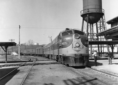 A black and white photograph of a train at a station, featuring a locomotive with the number 4035, surrounded by tracks, a water tower, and a few people nearby.