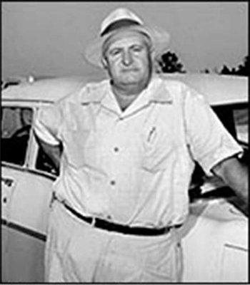 A man in a white shirt and hat standing next to a vintage car.