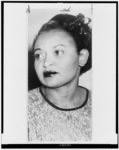 A black and white portrait of a woman with styled hair, wearing a textured top and looking to the side.