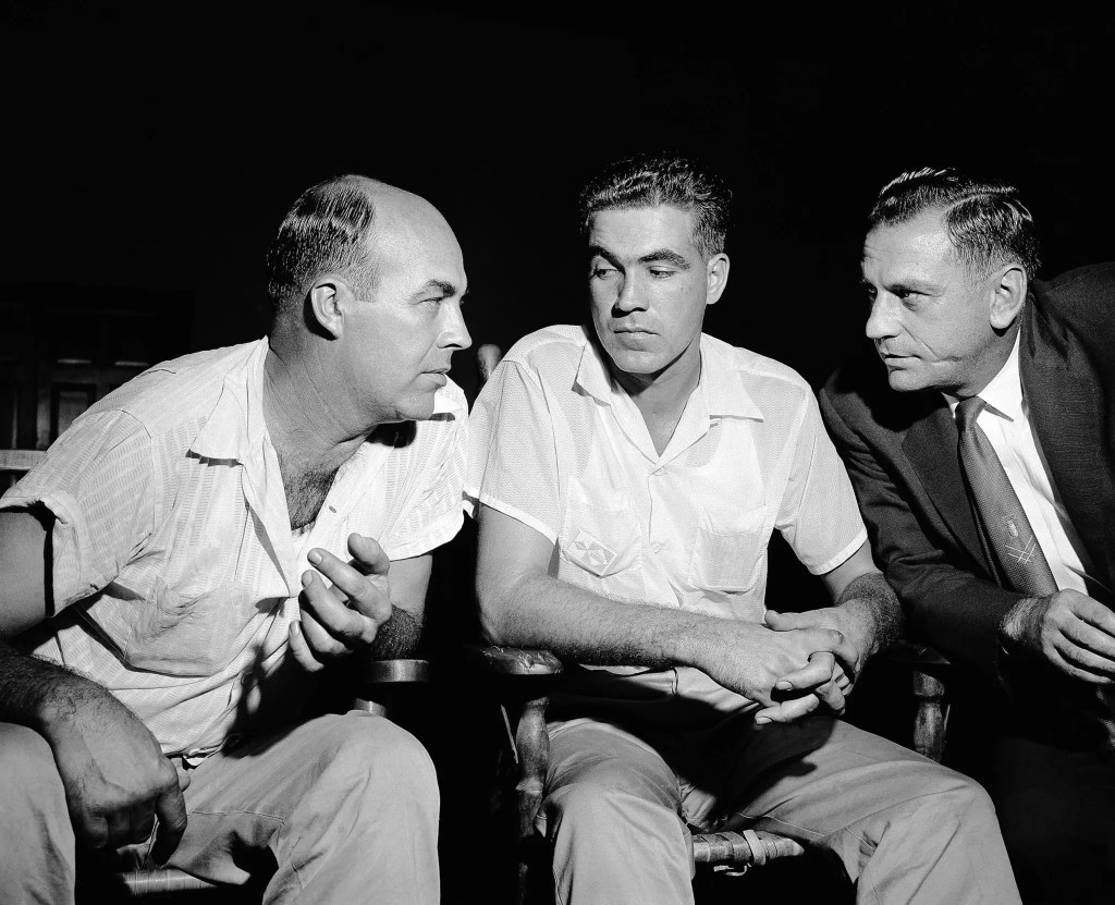 Three men seated, engaged in a serious discussion, with a dark background.