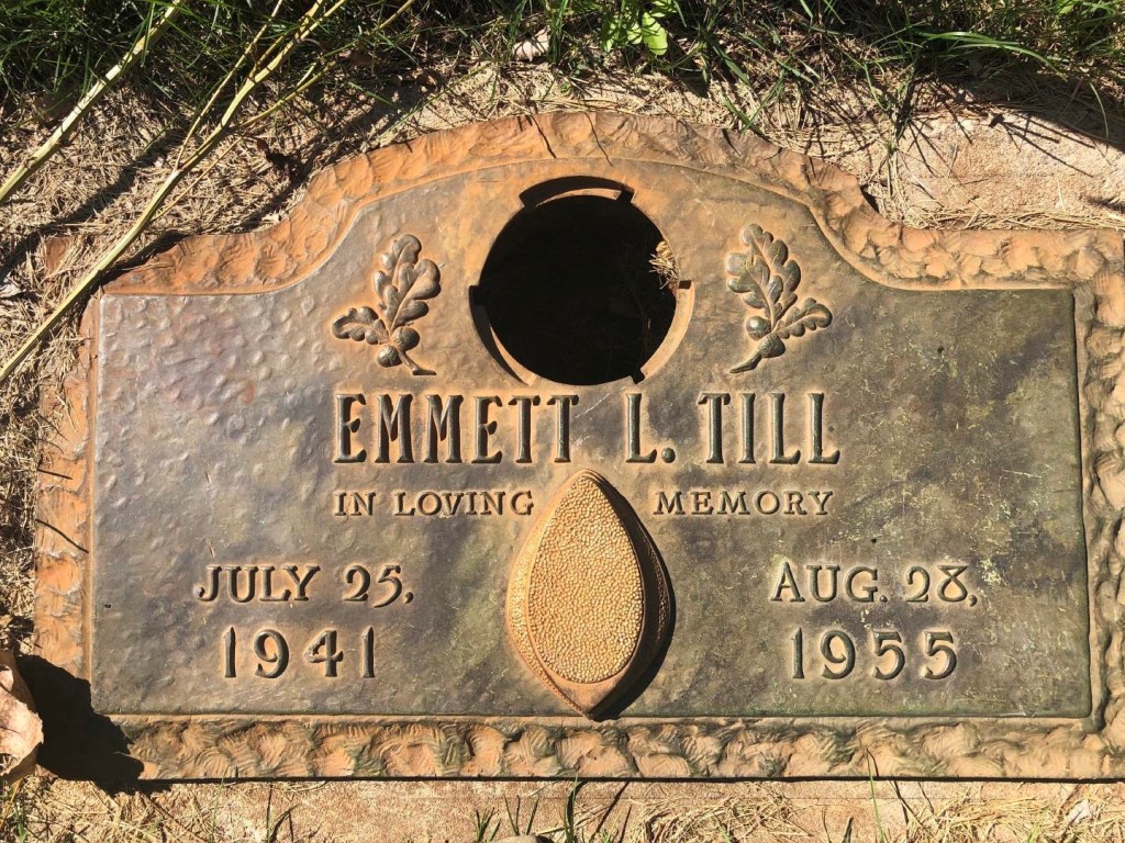 Gravestone of Emmett L. Till, engraved with his birth date, July 25, 1941, and death date, August 28, 1955, surrounded by greenery.
