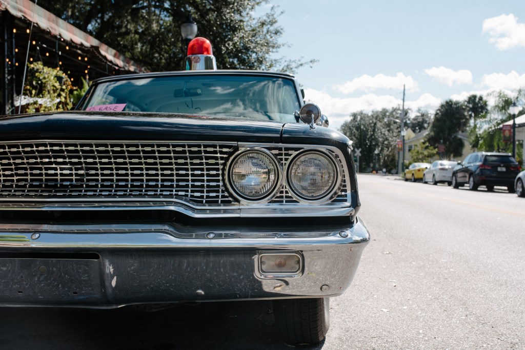 Front view of a vintage black police car with a red light on top, parked on a sunny street.